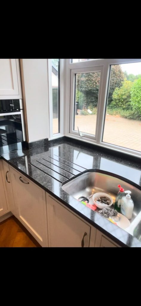 Grey granite worktop and drainer grooves beside a kitchen window, restored to a clean gloss