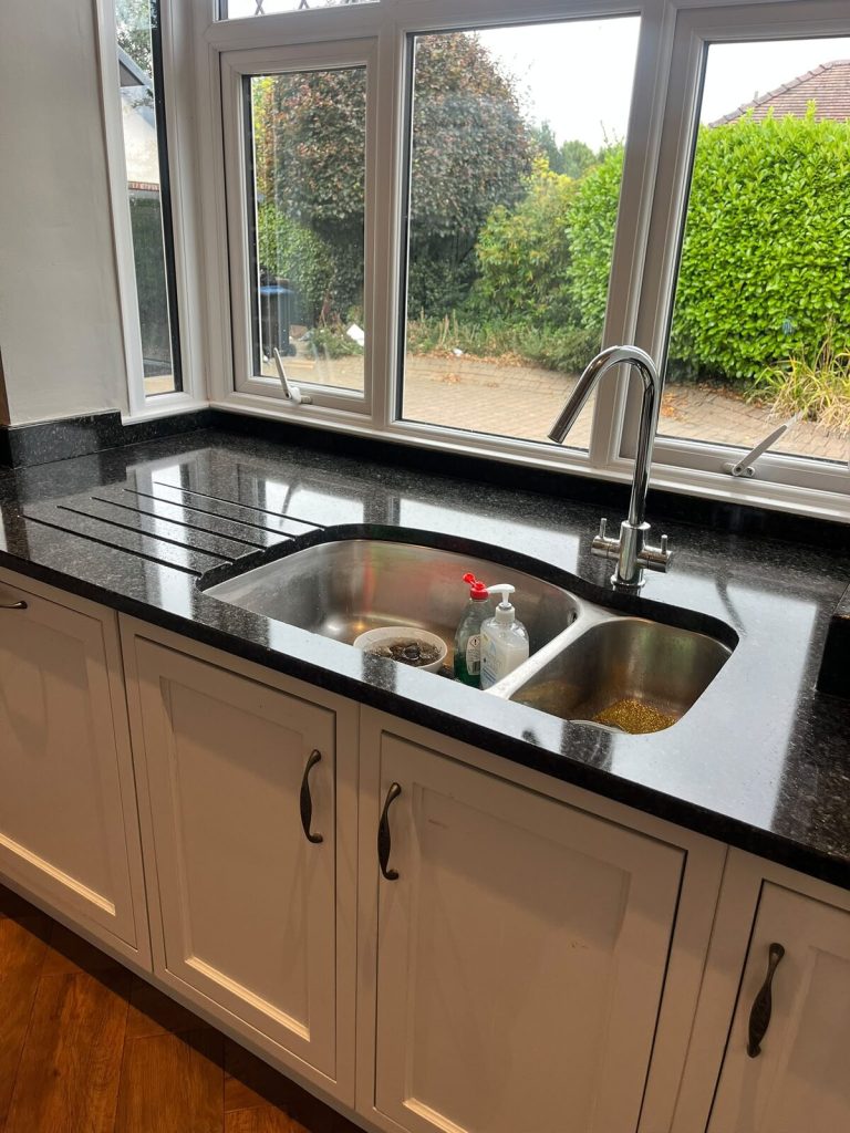 Restored granite worktop running around a double kitchen sink, reflecting the window light