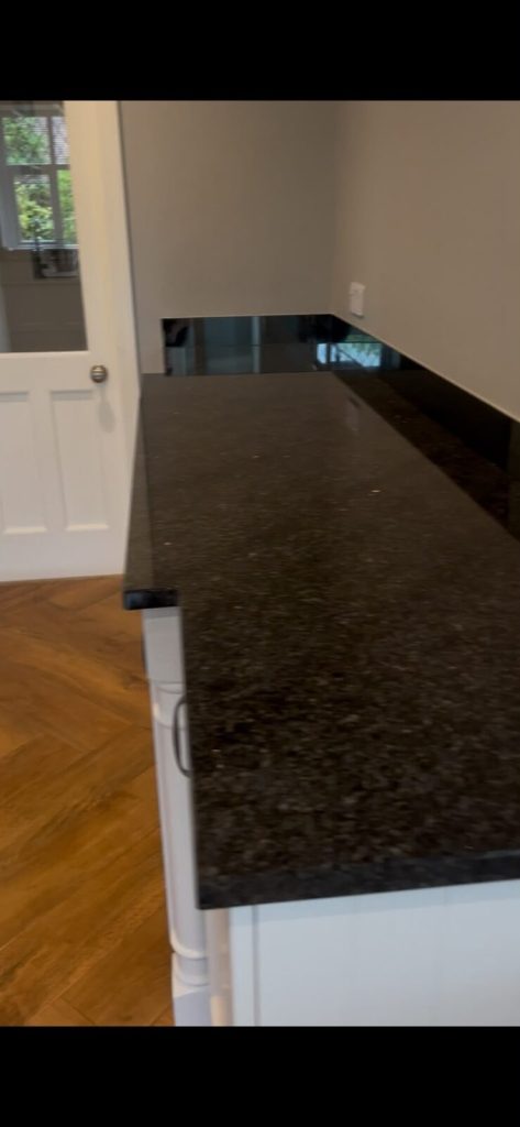 Dark granite worktop polished to a mirror gloss, reflecting a doorway and window