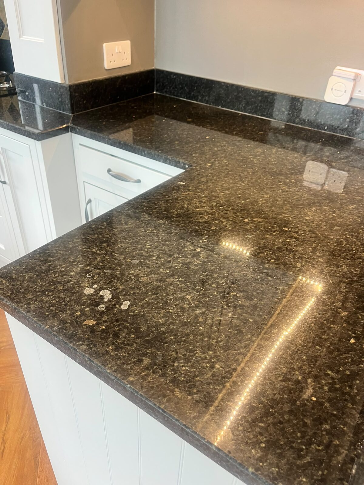 Dark granite kitchen worktop with dull patches and white water marks before restoration